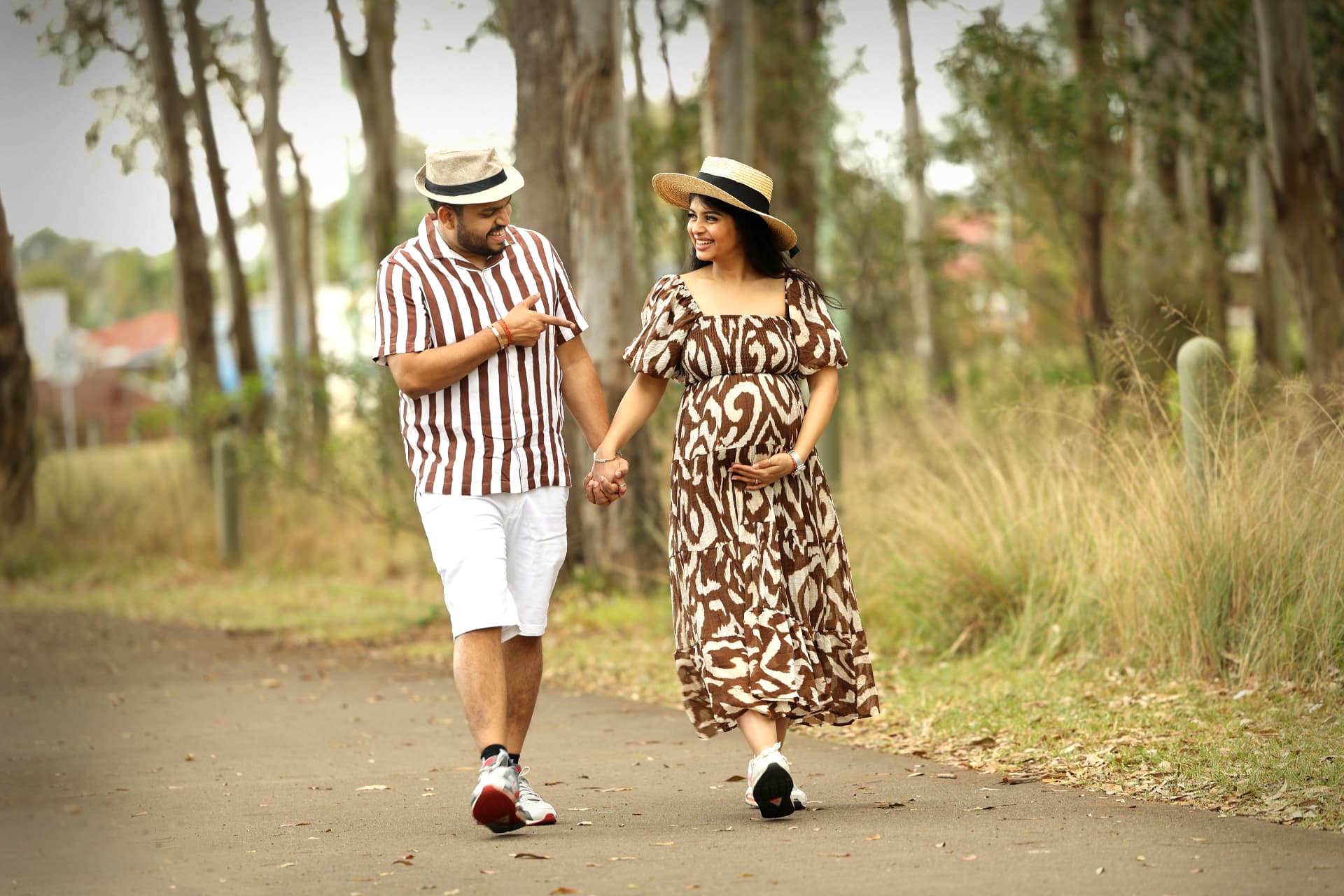 Expectant couple walking hand in hand on a tree-lined path, the mother-to-be resting her hand on her bump